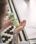 Person holding a green tube labeled 'hej' with a blurred background