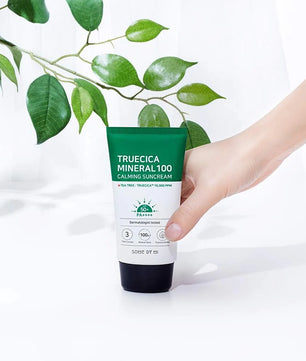 Hand holding a tube of Truecica Mineral 100 Calming Suncream with green leaves in the background