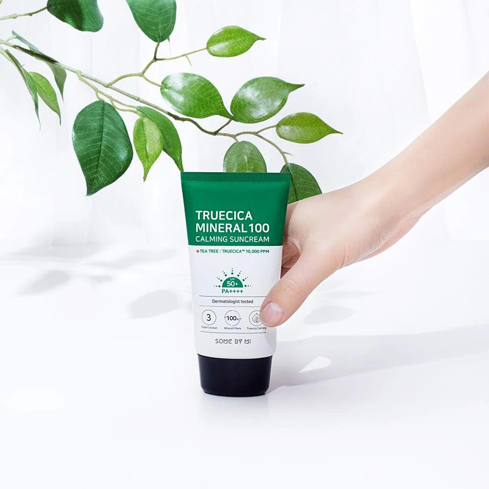 Hand holding a tube of Truecica Mineral 100 Calming Suncream with green leaves in the background