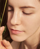 Close-up of a woman's face with eyes closed, holding a blade of grass.