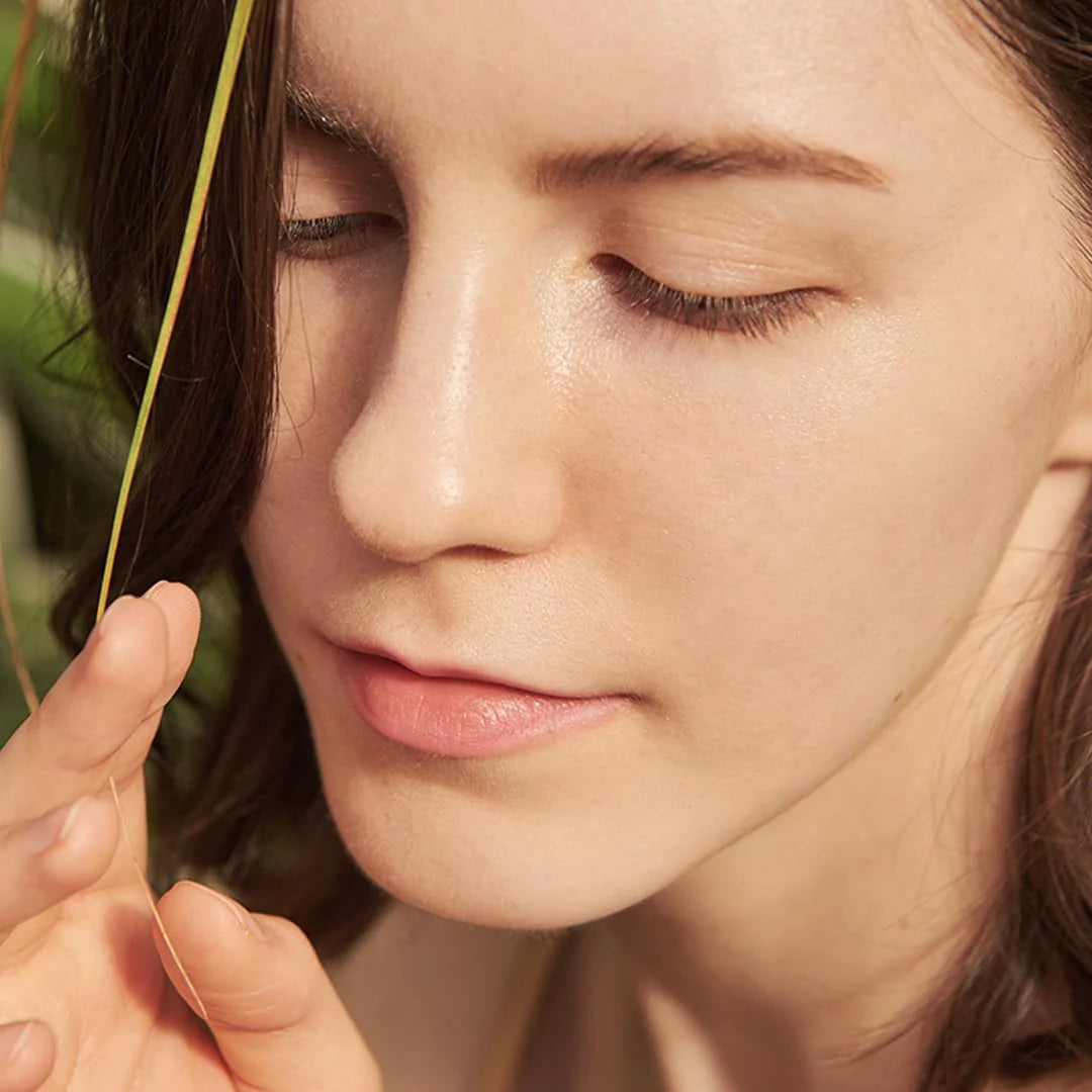 Close-up of a woman's face with eyes closed, holding a blade of grass.