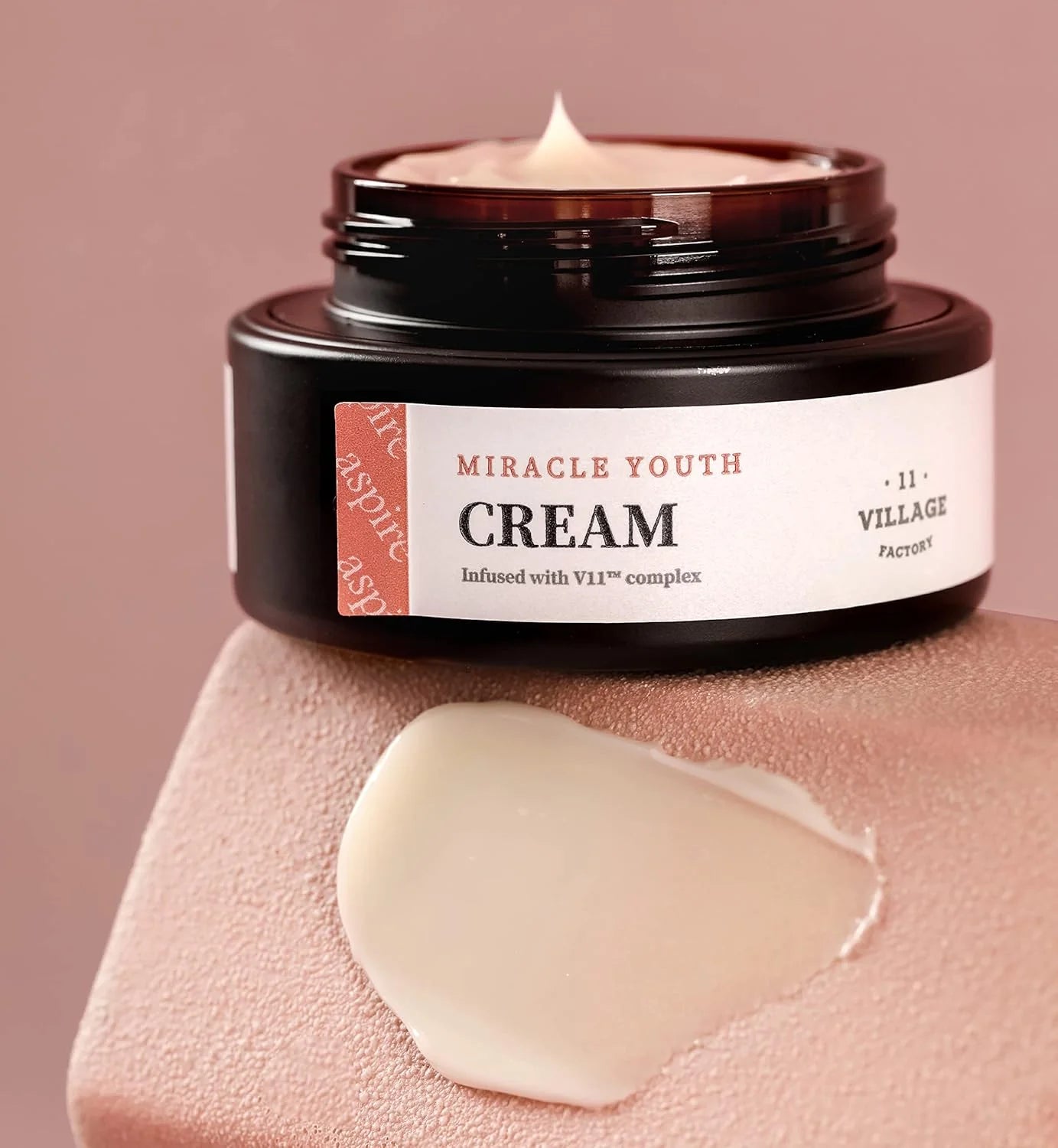 Jar of 'Miracle Youth Cream' with a swatch on a pink background