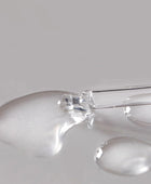 Glass dropper with clear liquid on a gray background