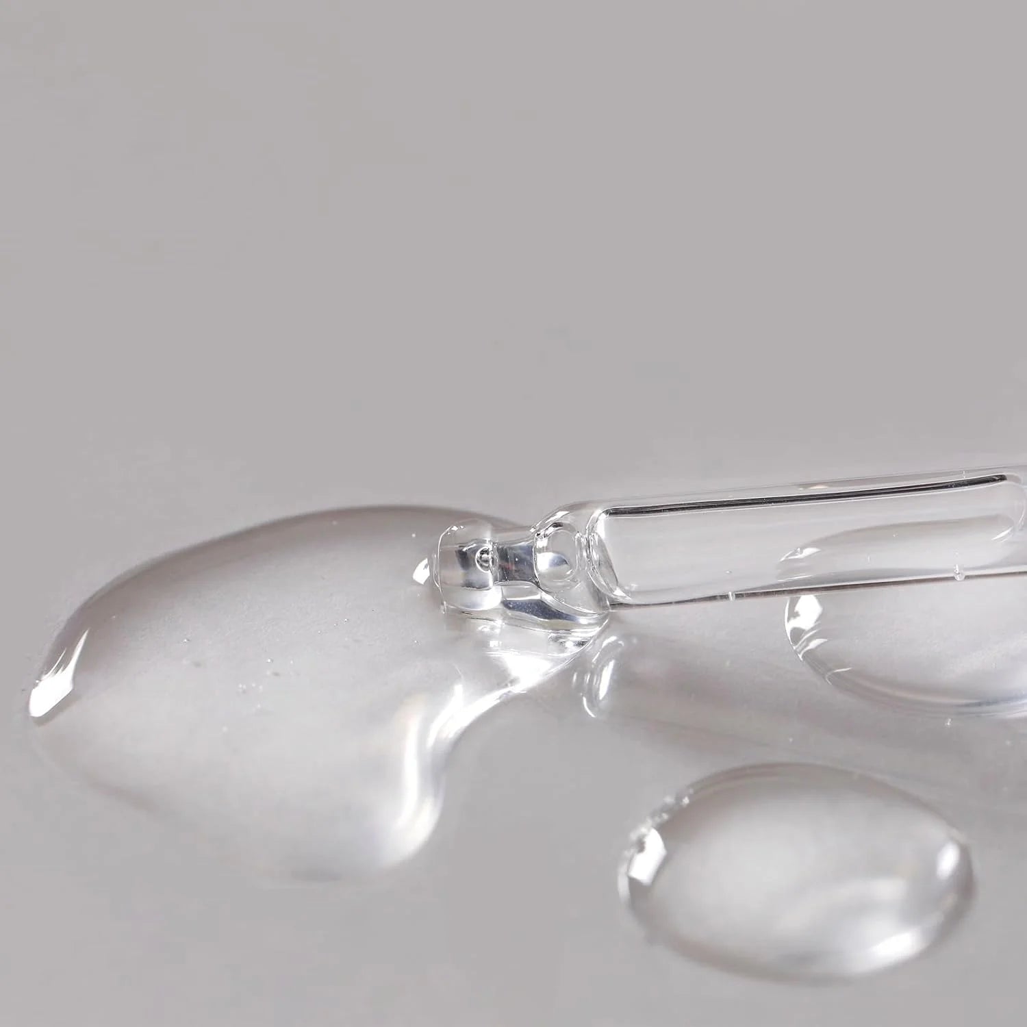 Glass dropper with clear liquid on a gray background