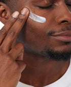 Man applying cream to his face with a neutral background