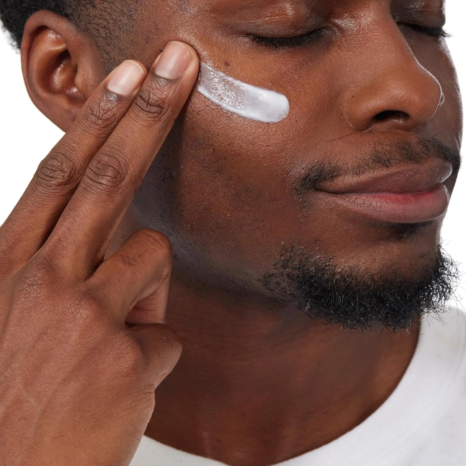 Man applying cream to his face with a neutral background