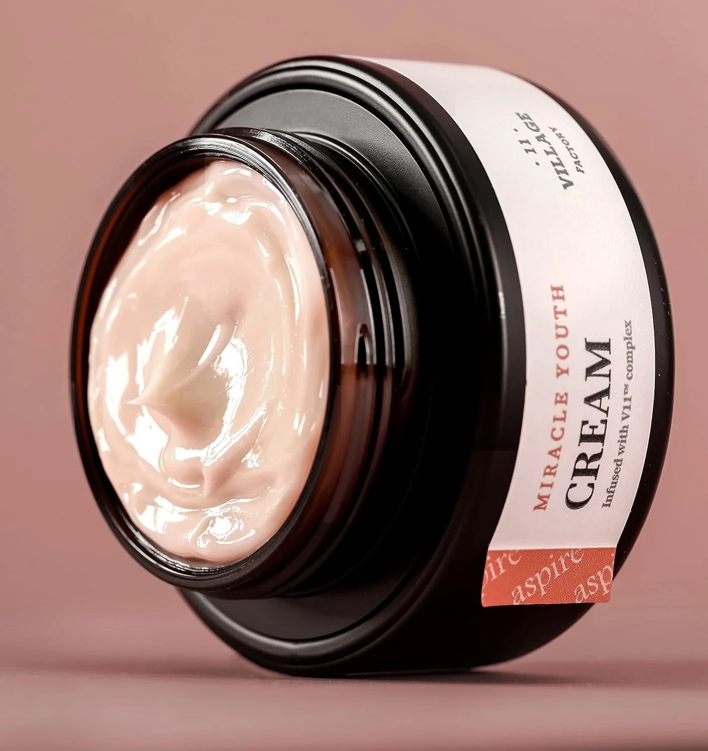 Jar of 'Miracle Youth Cream' with visible cream inside on a pink background